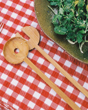 Load image into Gallery viewer, A set of hand carved salad servers sitting on a red and white table cloth next to a green salad