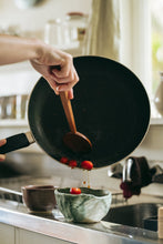 Load image into Gallery viewer, A hand carved spoon heating cherry tomato in a pan