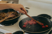 Load image into Gallery viewer, A hand carved spoon heating cherry tomato in a pan.