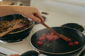 A hand carved spoon heating cherry tomato in a pan.