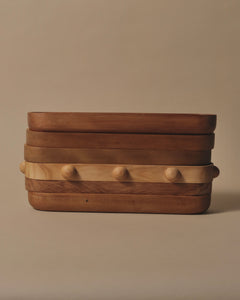 A stack of Long Trays in Rimu, Swamp Kauri and Matai, one tray has 8 half spheres around the edge in equal distance from each other