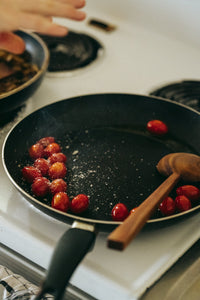 A hand carved spoon heating cherry tomato in a pan