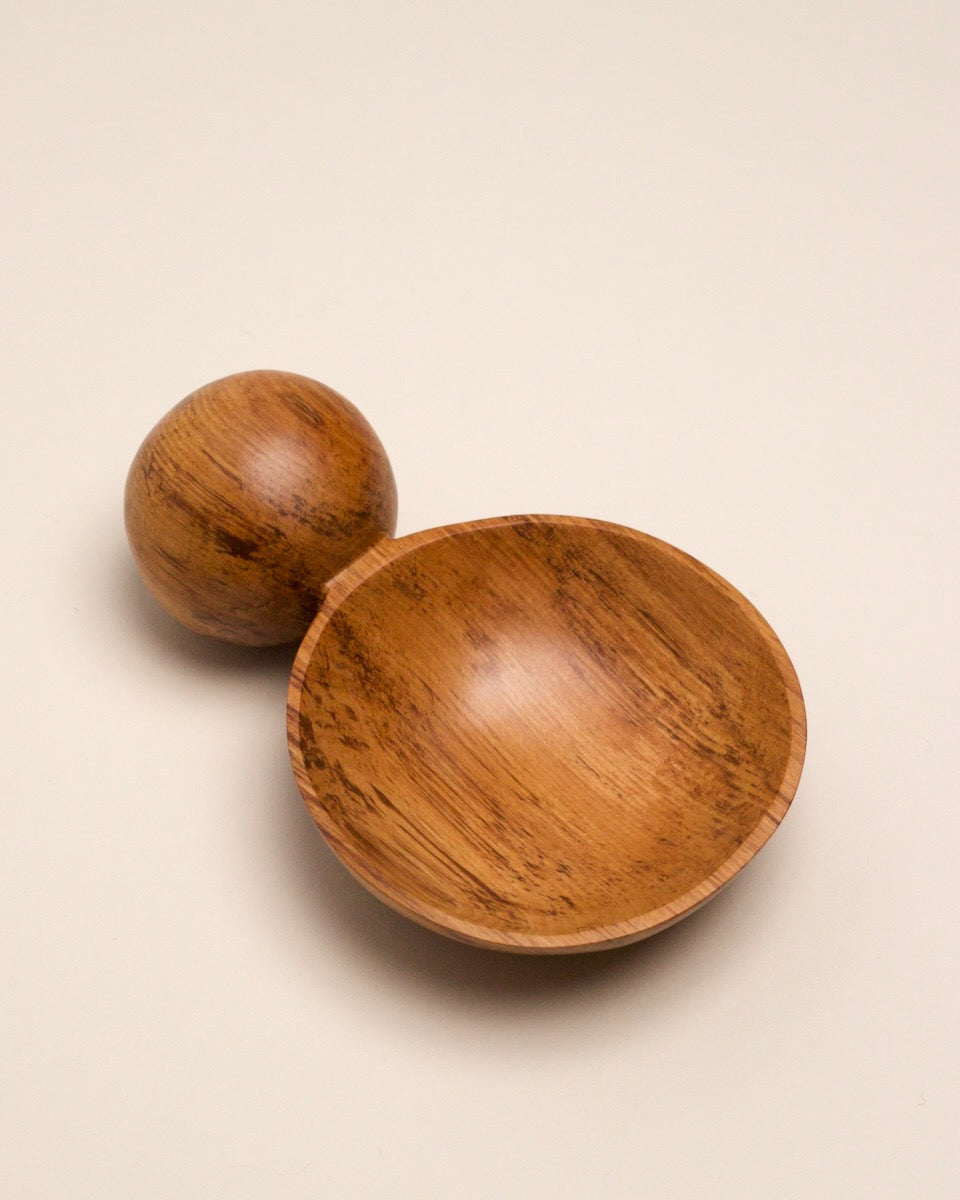 A hand carved spoon made of rimu on a white back ground, the spoon bowl is deep and round and the handle is a hand carved sphere.