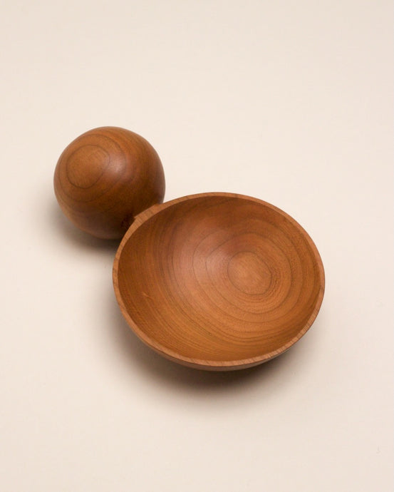 A hand carved spoon made of rosewood on a white back ground, the spoon bowl is deep and round and the handle is a hand carved sphere.