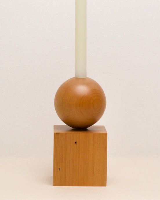 Hand-carved candle holder made from kauri wood, featuring a spherical base atop a square block.